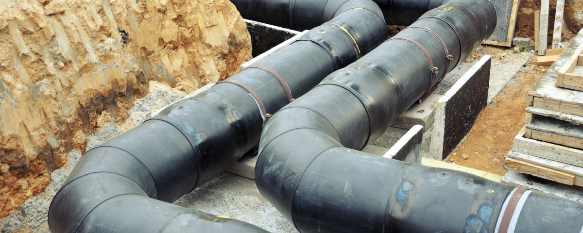 The process of laying of engineering heating systems. Two turning black plastic pipes in sandy trench.